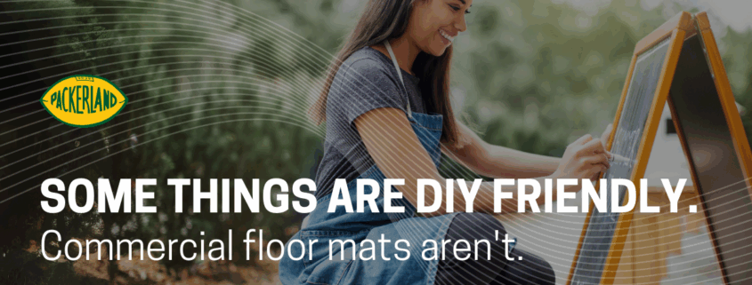 A woman with brown, shoulder length hair, wearing jeans and a grey t-shirt kneels on the ground in front of a chalkboard. She is writing the specials of the day on the chalkboard. Over the image, text reads, "Some things are DIY friendly. Your commercial floor mats aren't."