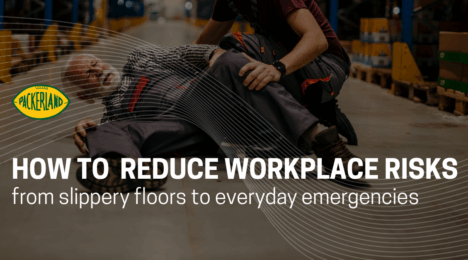 A man in his 60's lays on the floor clutching his legs and hips, his face visibly in pain. Next to him, another man whose face is not shown is crouching down to try to assist the injured man. He is wearing a red apron. Behind them are pallets of items that are slightly blurred, suggesting they are at work.