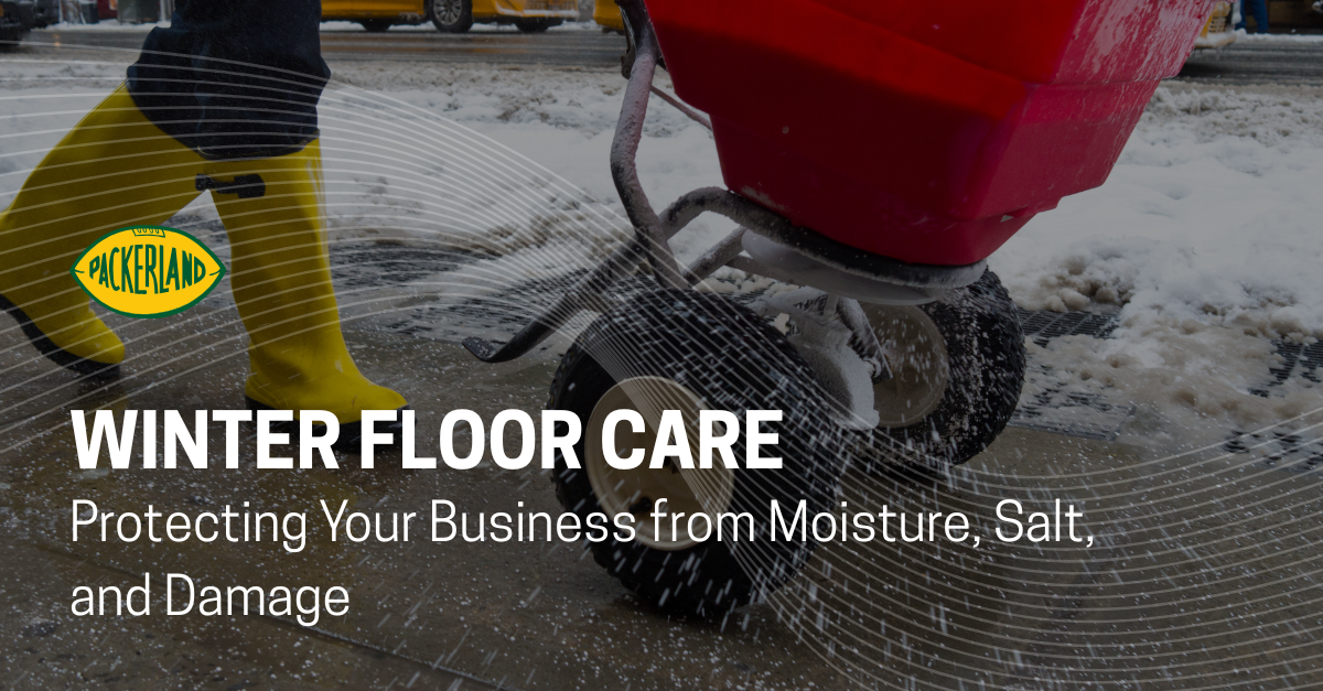 A red salt spreader is being pushed by a woman who is wearing yellow boots. Only her legs, wearing jeans, are shown in the frame. In the background, a salt covered sidewalk is beginning to appear from under the melting snow.