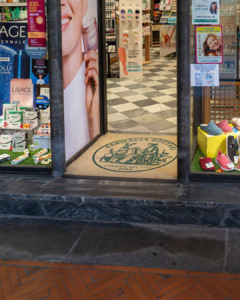Custom logo mat for Farmacia Bottari placed at the storefront entrance with checkered tile flooring visible inside.