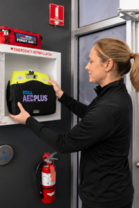 workplace aed access A woman wearing a black shirt pulling an AED out of a mounted wall cabinet