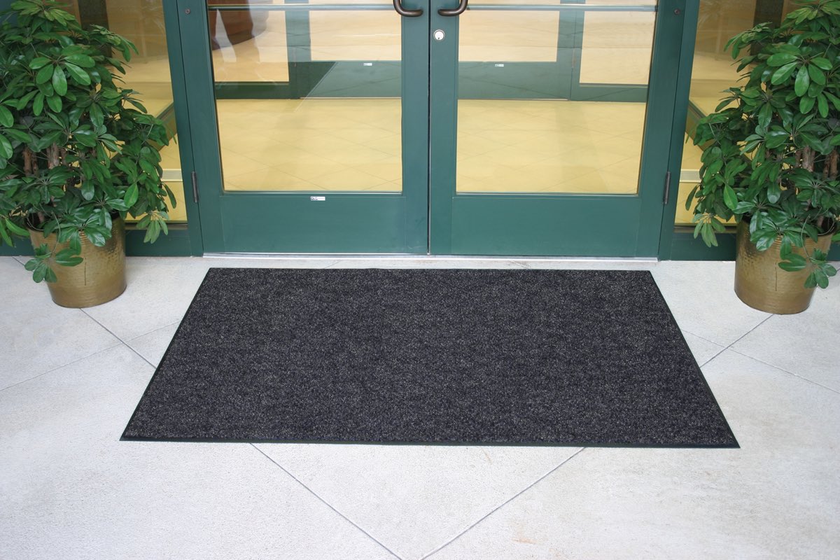 A charcoal brush entrance mat in front of green glass double doors.