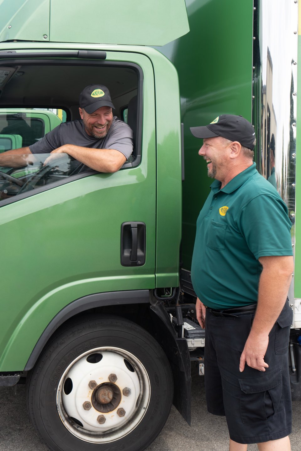 Two Packerland team members laughing beside a green Packerland delivery truck.