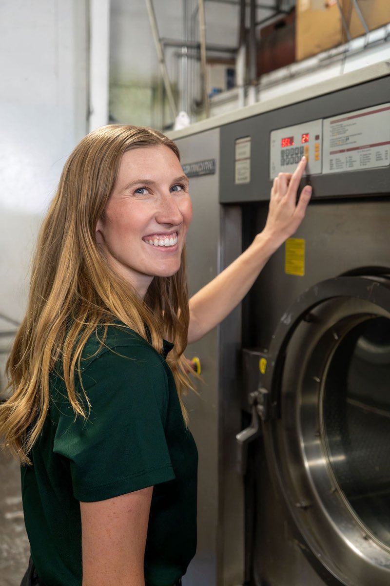 A Packerland team member starts an industrial washer and smiles at the camera.